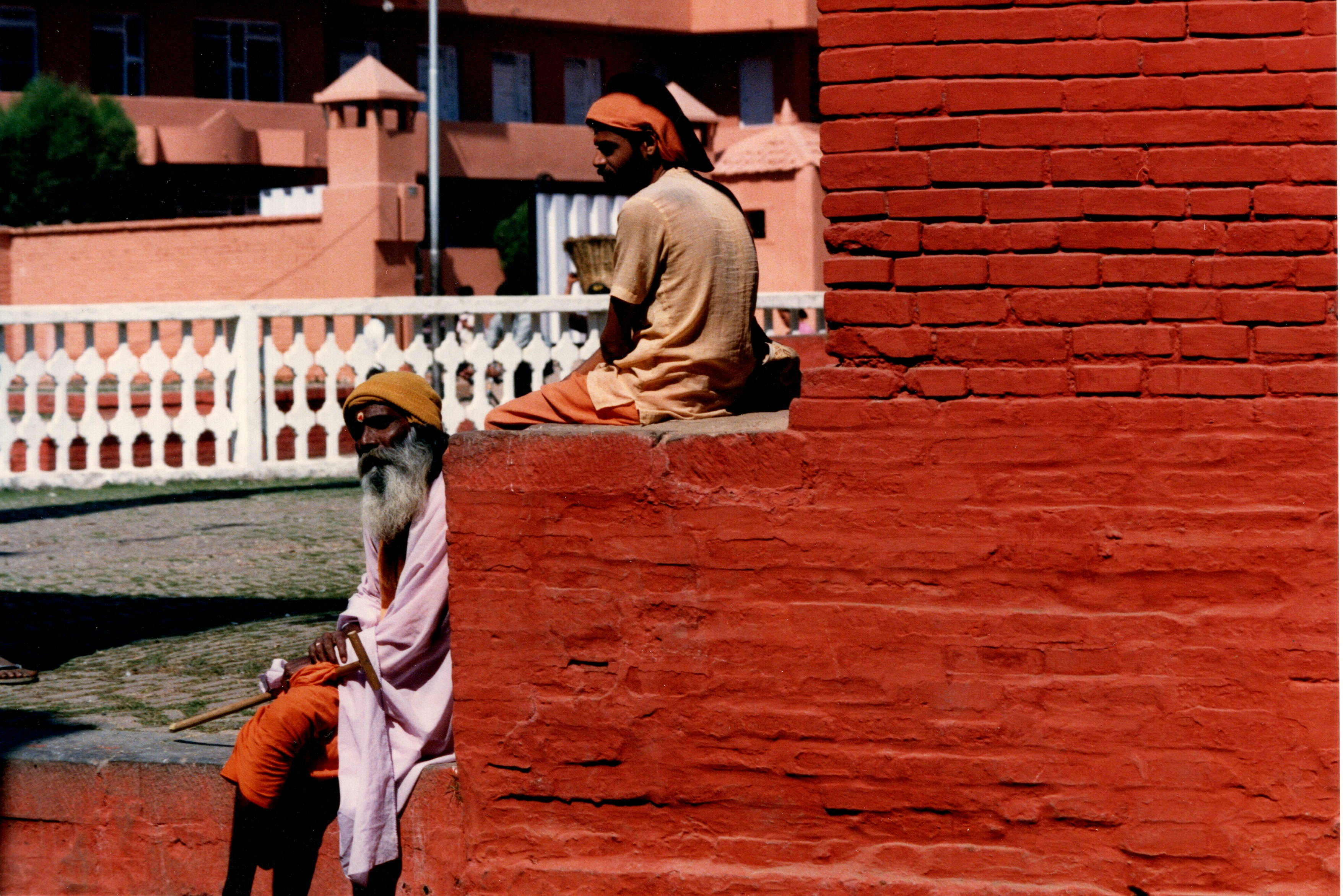 Two Hindu sadhus resting against a red brick wall at a sacred site in Varanasi